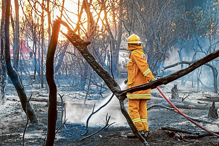 Mopping up: A fireman douses burning embers after a wind change brought relief to Crib Point Monday week. Picture: Gary Sissons