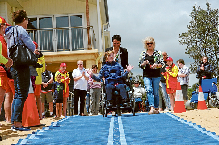 Ready to roll: Above, Karen Frankhauser, tries out the new beach matting at Mt Martha with Virginia Richardson and the mayor Bev Colomb (right) while, below, Cooper Smith gets a helping push towards the sea from his sister Pepper. Pictures: Keith Platt